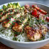 Grilled chimichurri chicken slices fanned over fluffy rice with vibrant cherry tomatoes, avocado, cucumber, and fresh herbs.