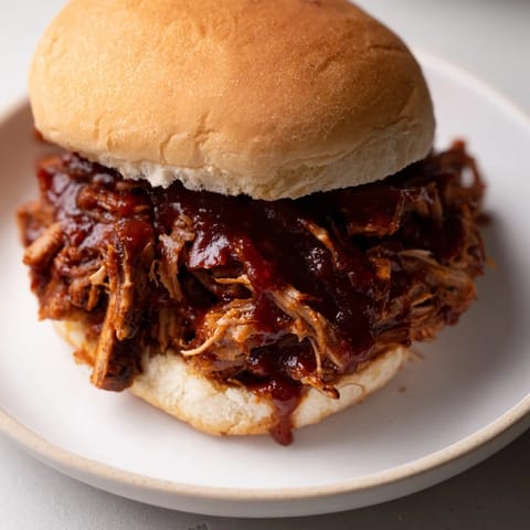 Warm, smoky pulled pork on a toasted bun, garnished with slaw for a perfect BBQ sandwich.