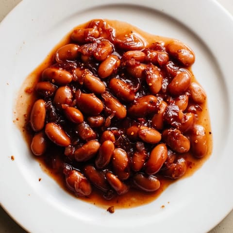 Close-up of golden-brown baked beans, a comforting American classic, served with crusty bread.