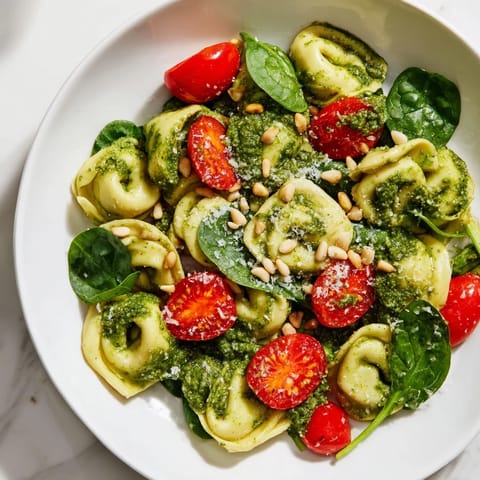 Vibrant pesto tortellini salad with juicy tomatoes and fresh spinach, perfect for any gathering.