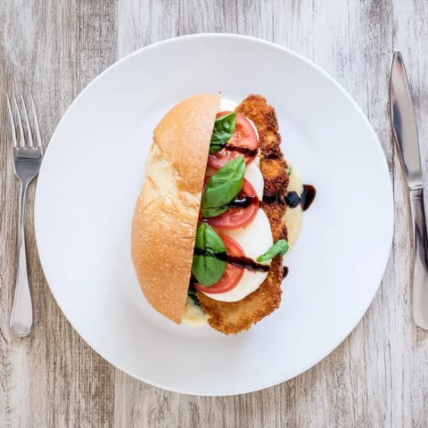 Crispy Chicken Caprese Sandwich on a rustic board, drizzled with balsamic glaze and served with a side salad.