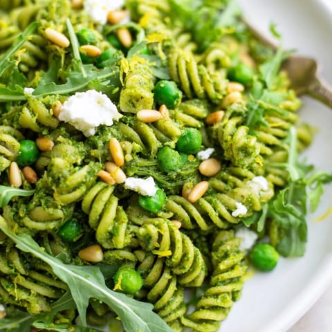 A vibrant bowl of Spring Green Pesto Pasta Salad featuring fusilli, peas, and arugula tossed in creamy basil pesto.
