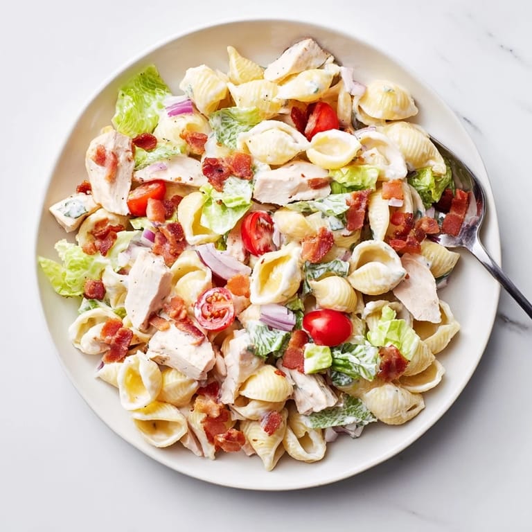 A close-up of BLT Chicken Pasta Salad, featuring pasta shells, romaine lettuce, and diced grilled chicken tossed in mayo.  
