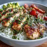 Grilled chimichurri chicken slices fanned over fluffy rice with vibrant cherry tomatoes, avocado, cucumber, and fresh herbs.