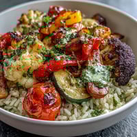 Rainbow Roasted Vegetable Bowl with vibrant, caramelized veggies over fluffy brown rice, drizzled with fresh herb sauce.